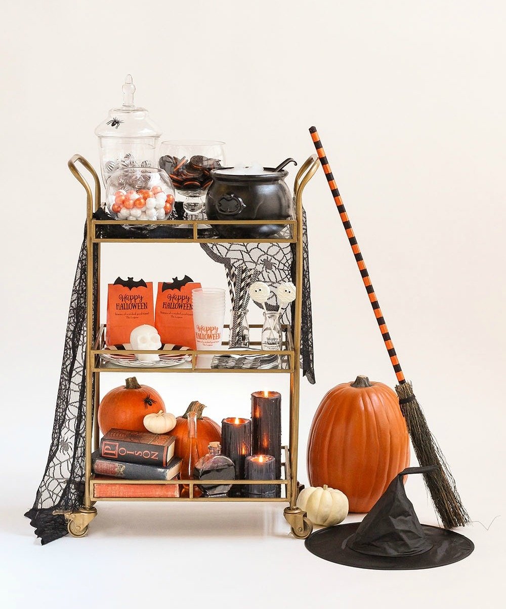 A Halloween bar cart with candy, cookies, pumpkins, a witch hat, witch broom, and other treats. 