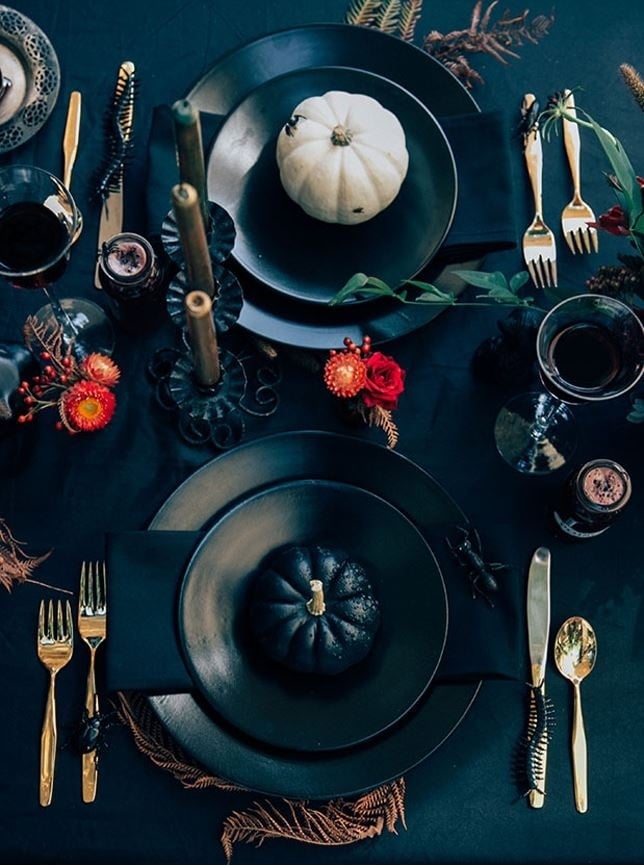 A black and red Halloween table scape with candles, black pumpkins, wine, and fake bugs. 
