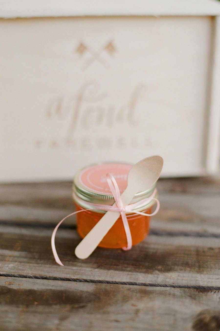 A peach jam wedding favor in a jar tied with ribbon and a wooden spoon. 